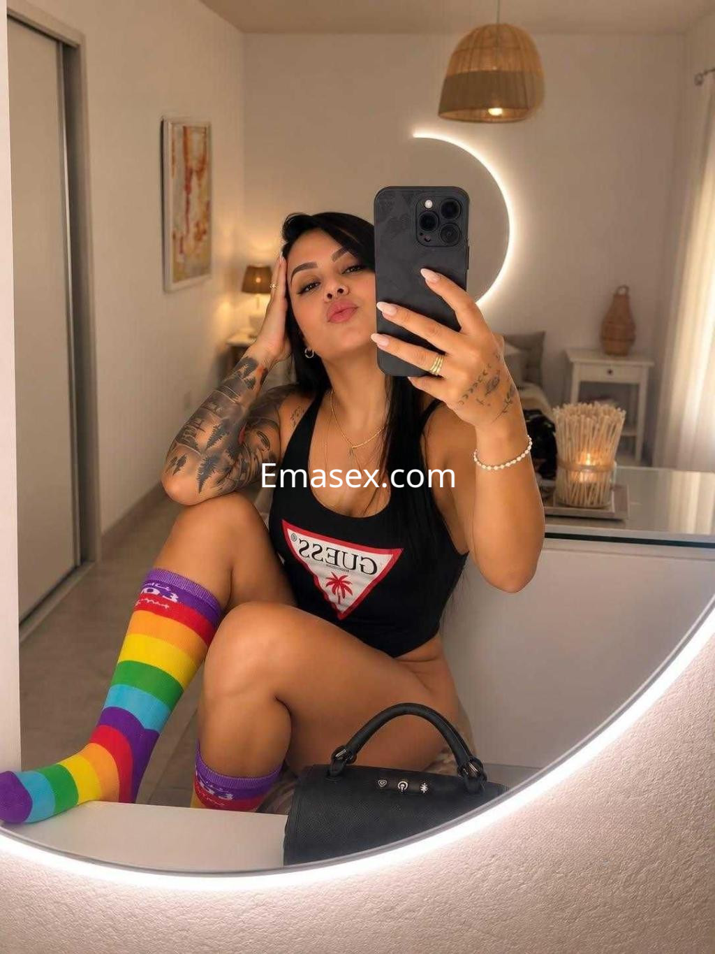 Escort en Tenerife, posando en un espejo con un top negro, calcetas de colores y un ambiente moderno y luminoso.