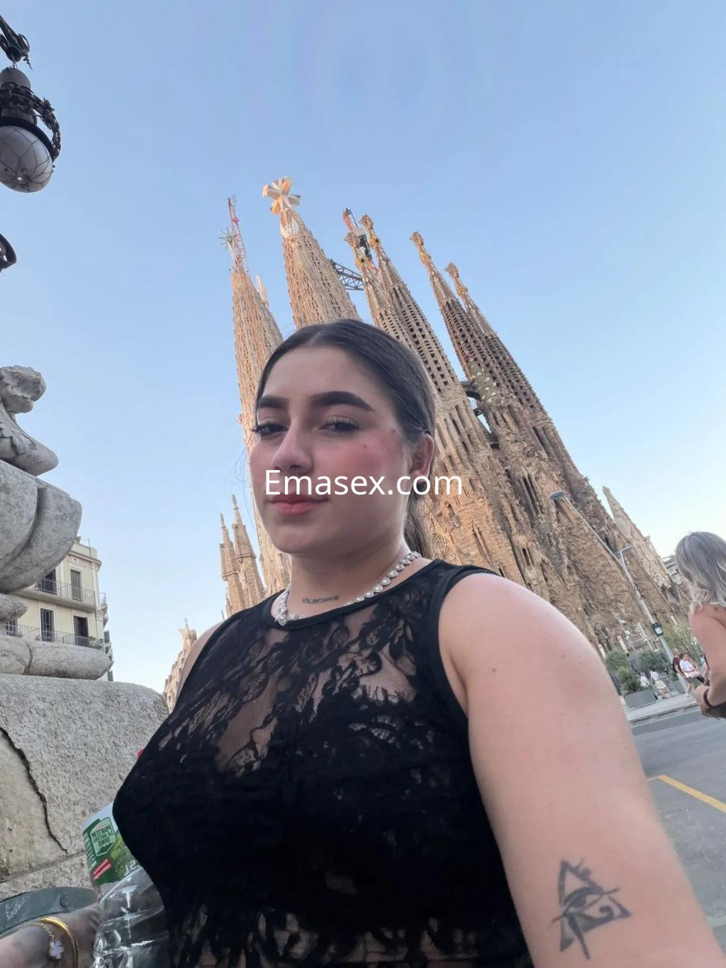 Puta con blusa de encaje negra posando frente a la Sagrada Familia en Valencia, luciendo un look elegante.