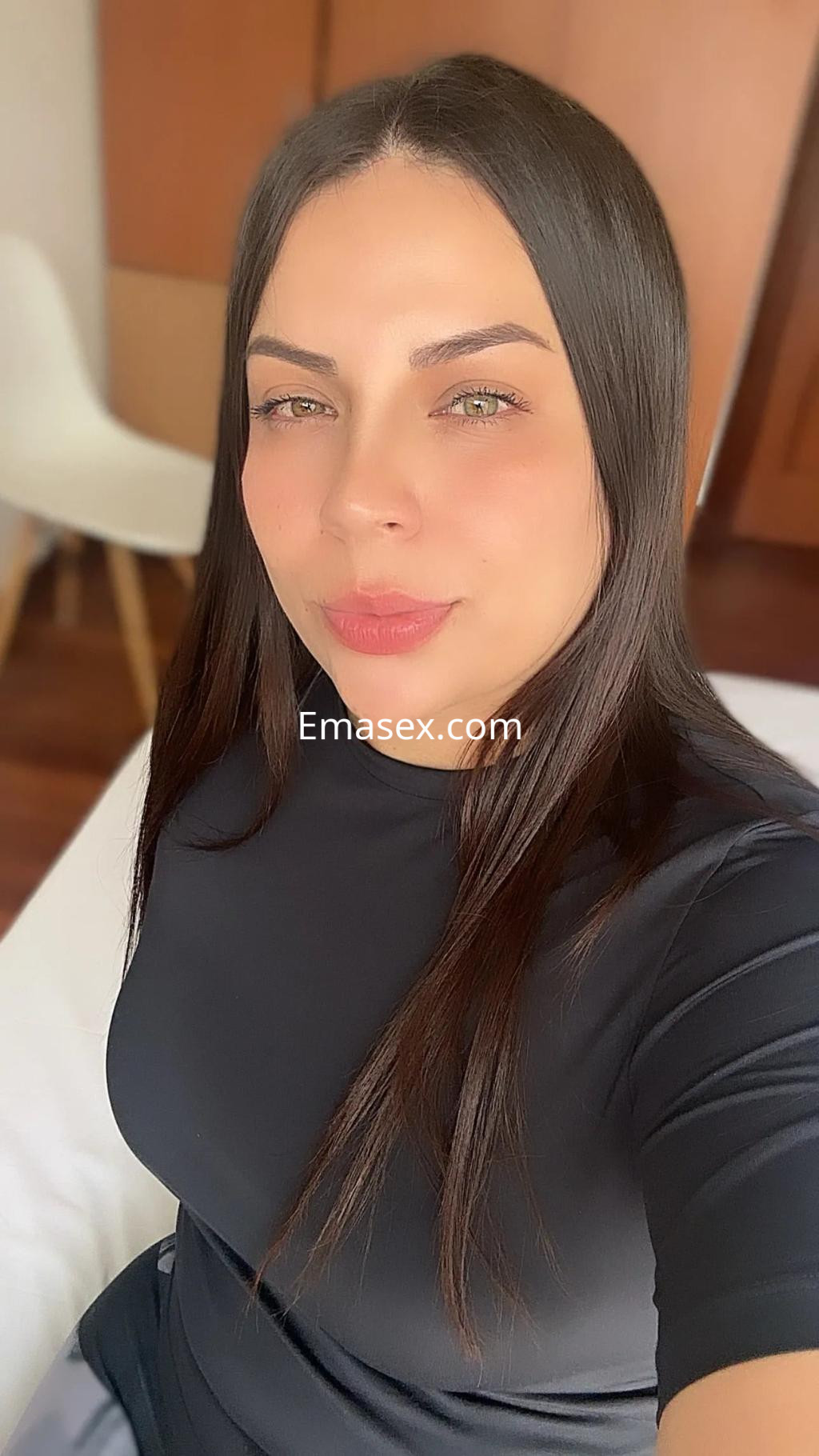 Puta en Coruña con cabello largo y lacio, usando una camiseta negra, posando en un entorno acogedor.