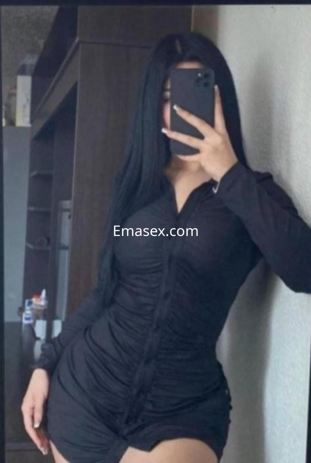 La escort se toma una selfie en un vestido negro ceñido con botones, mostrando su figura en Coruña.