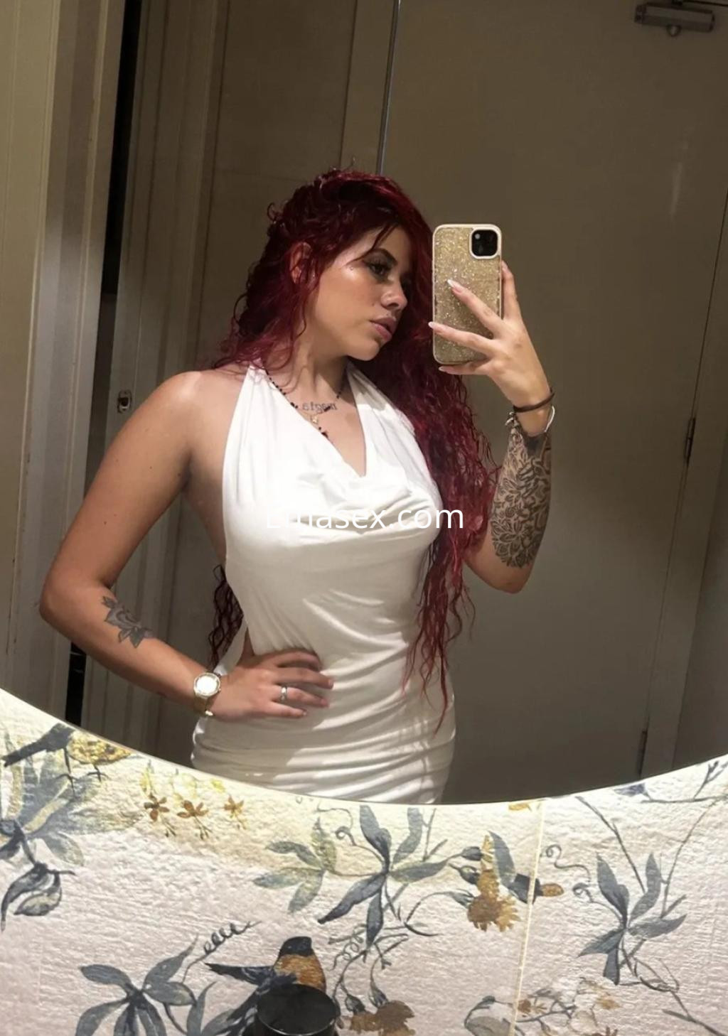 Escort con cabello rizado y rojo, luciendo un vestido blanco ajustado mientras se toma una selfie en Oviedo.
