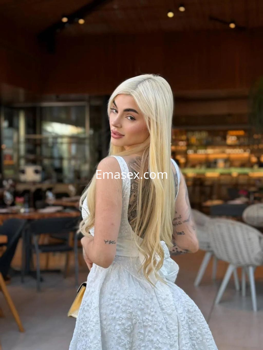 Puta con cabello rubio largo y liso, luciendo un vestido blanco en un moderno café de Madrid.