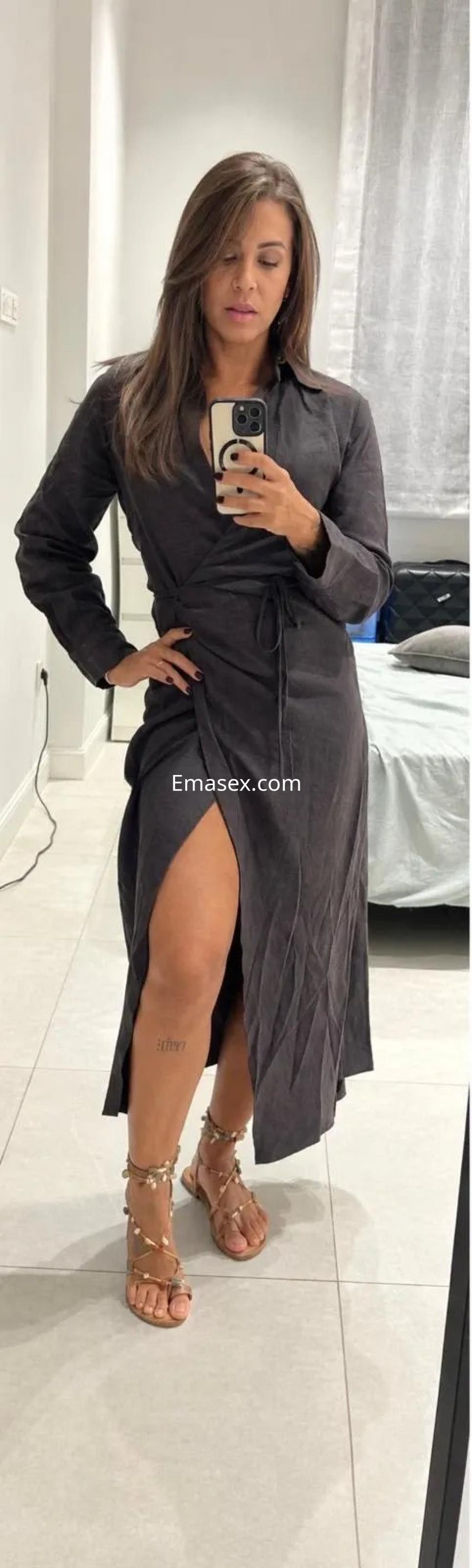 Escort en Málaga con cabello castaño y lacio, viste un vestido oscuro con abertura y sandalias elegantes.