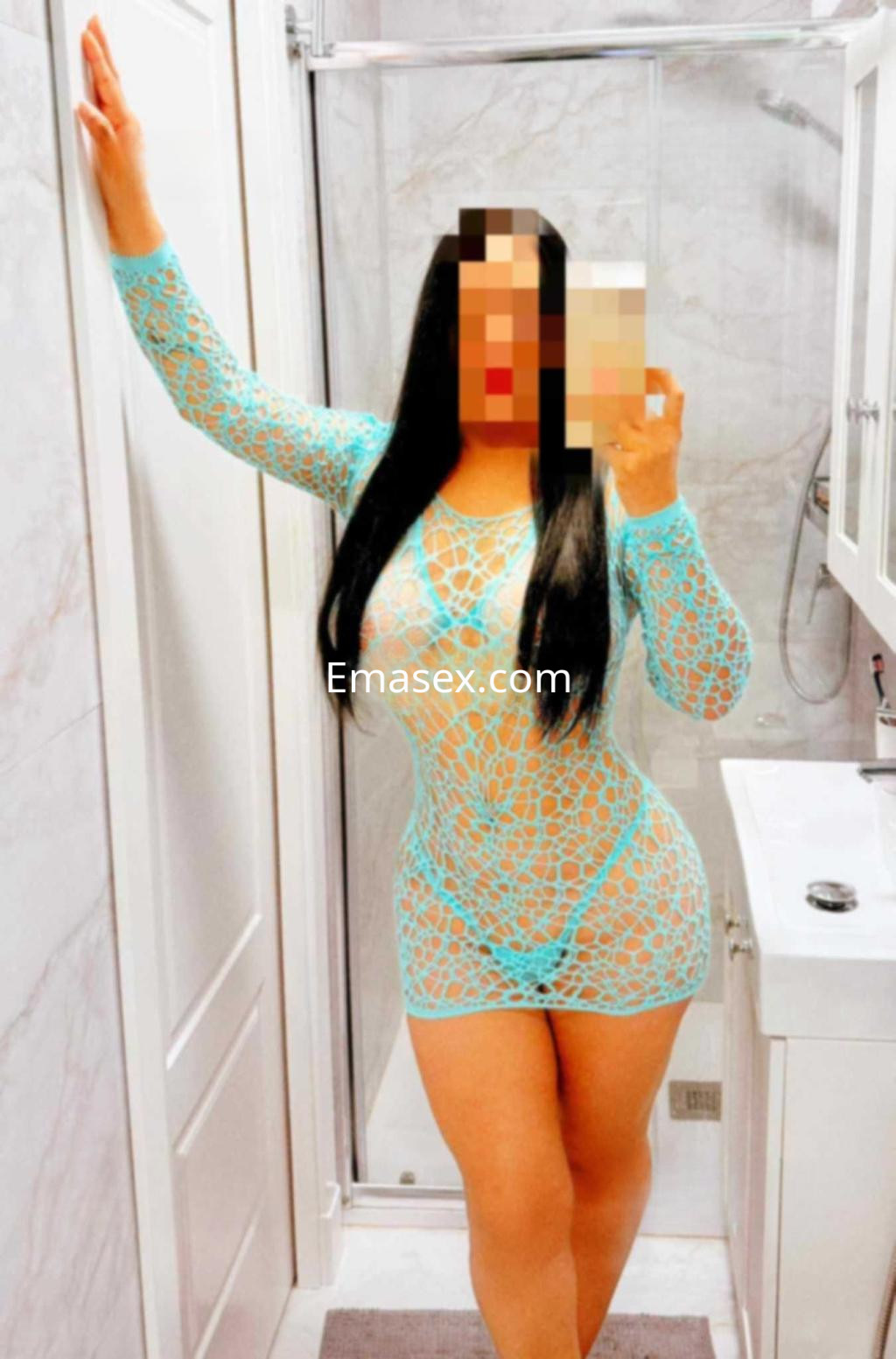 Puta con vestido de encaje azul, posando en un baño moderno de Málaga, mostrando su figura curvilínea.
