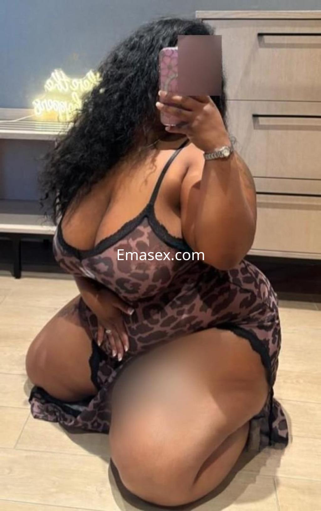 Escort en Sevilla, con cabello rizado y vestido de leopardo, posando de rodillas frente a un espejo.