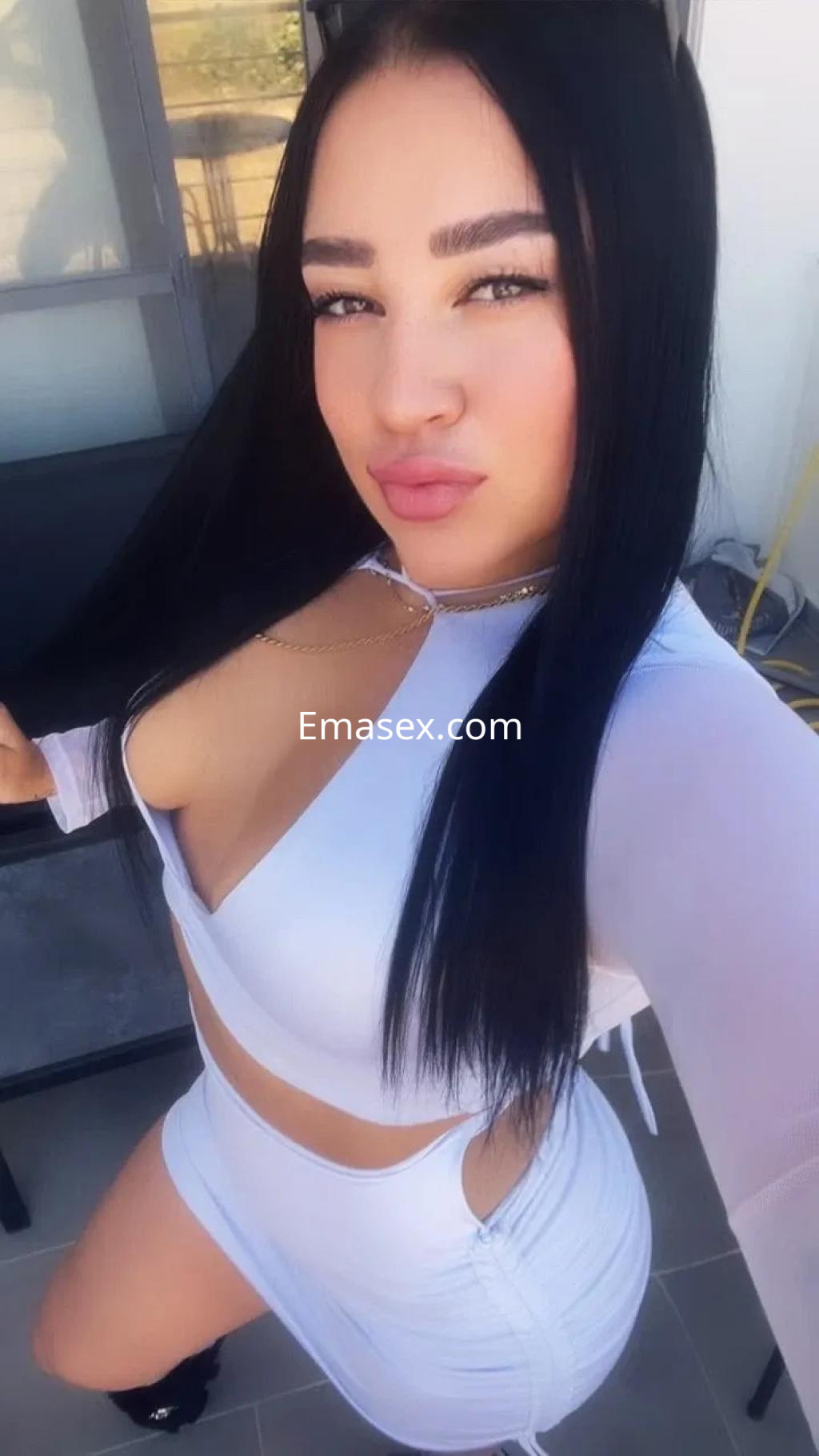 Escort en Sevilla posando con un conjunto blanco, de top y falda corta, con cabello largo y lacio.
