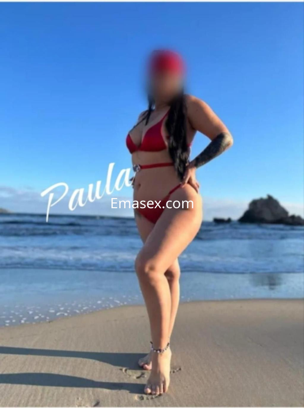 Puta en la playa de Málaga, luciendo un bikini rojo y con el cabello largo y oscuro, posando junto al mar.