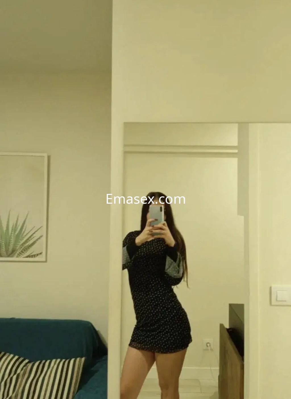 Escort en Alicante posa frente al espejo, luciendo un vestido negro con puntos y cabello largo.