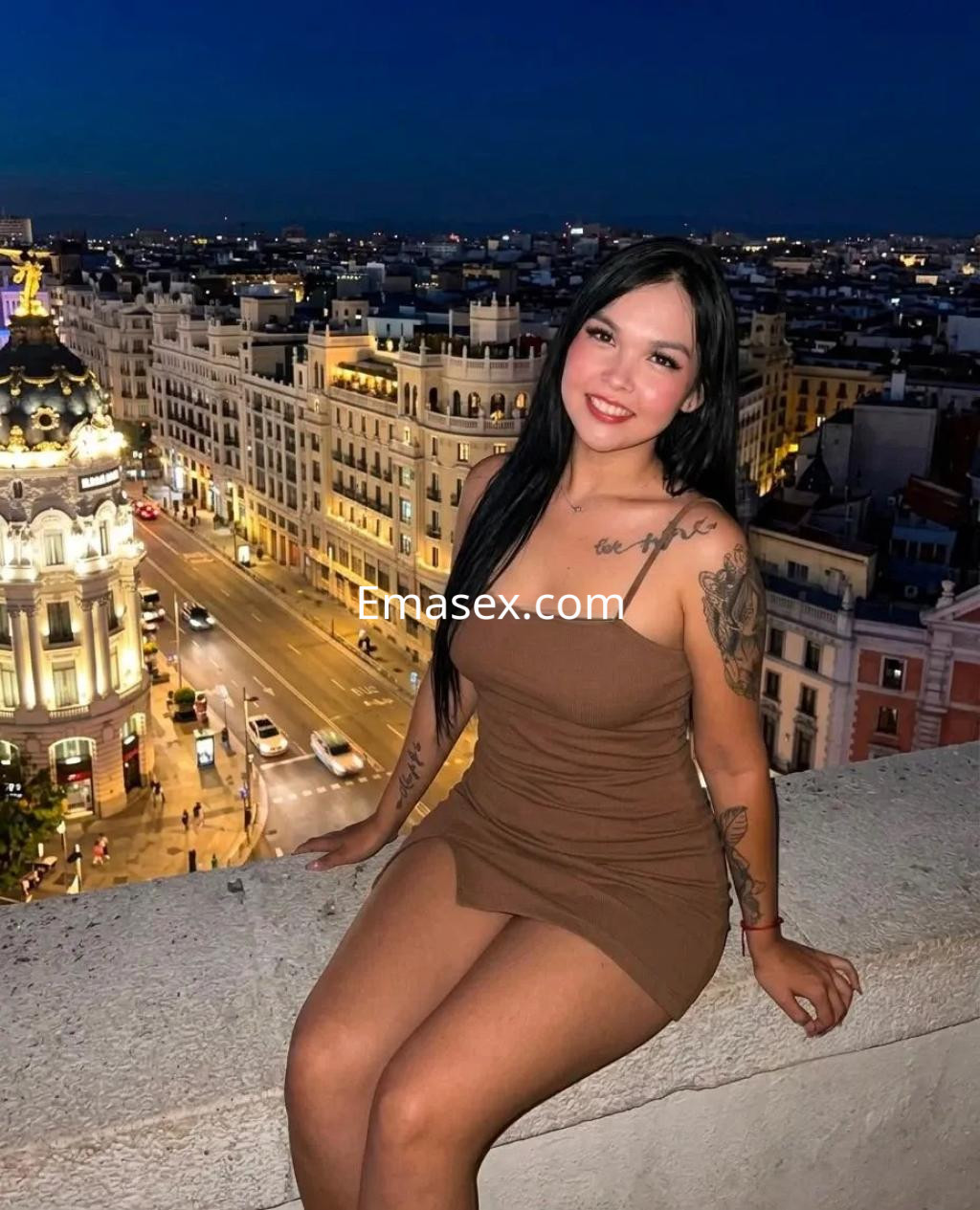 Puta en Bilbao posando en una azotea al atardecer, viste un vestido marrón ajustado y tiene cabello largo y lacio.
