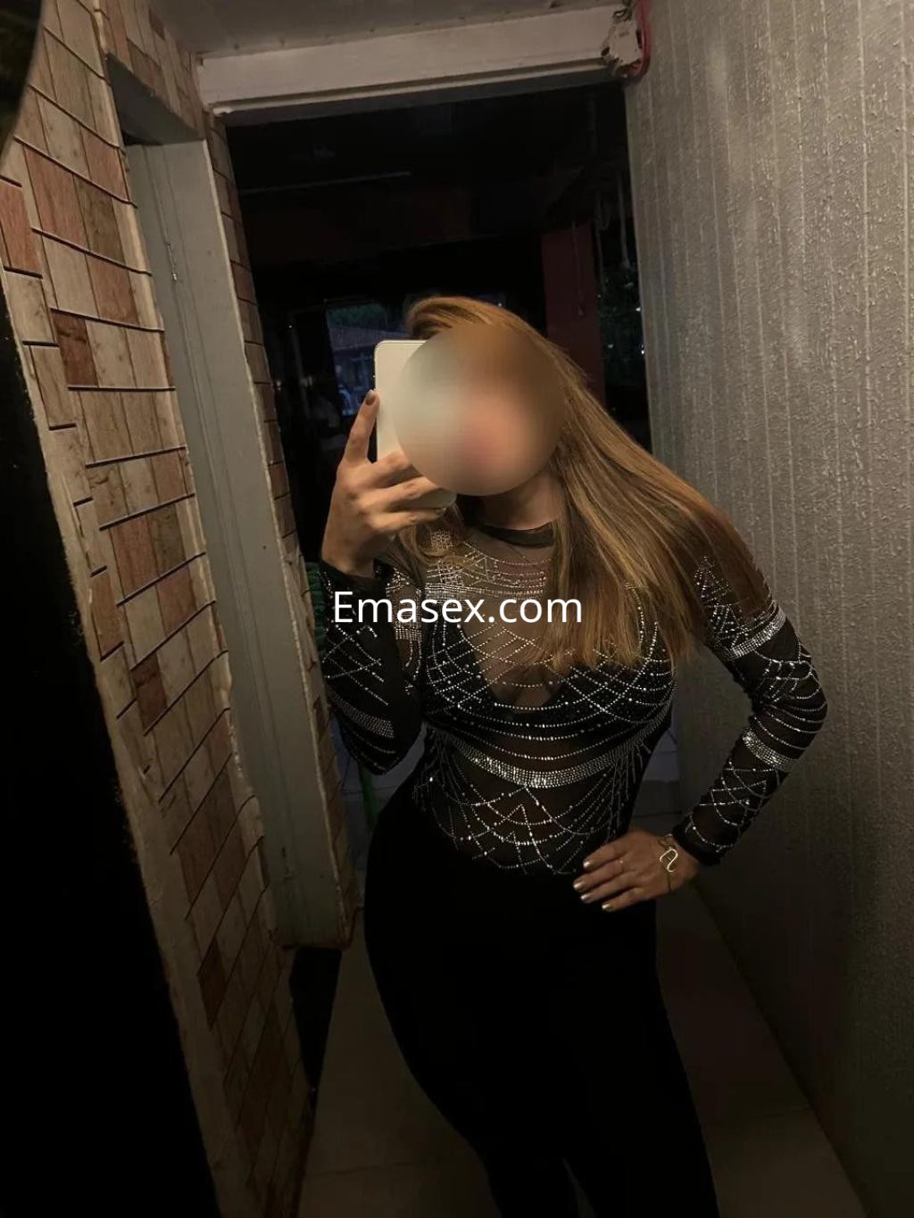 Escort en Valencia posando frente al espejo con un top de malla negra brillante y pantalones ajustados.