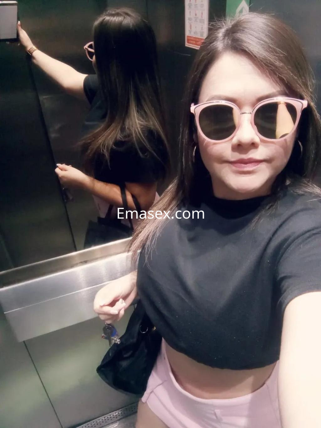 Puta posando en un ascensor con gafas de sol rosas, blusa negra y falda corta en Coruña.