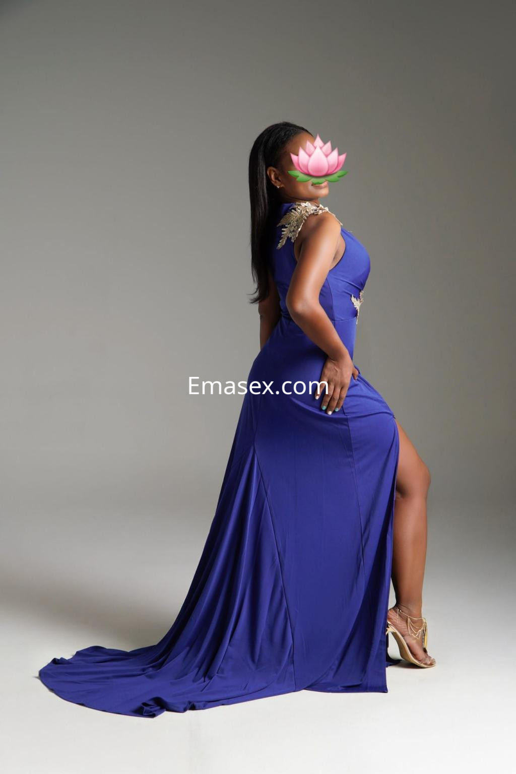 Escort en Zaragoza luciendo un vestido largo azul con detalles brillantes, posando de perfil con un fondo neutro.