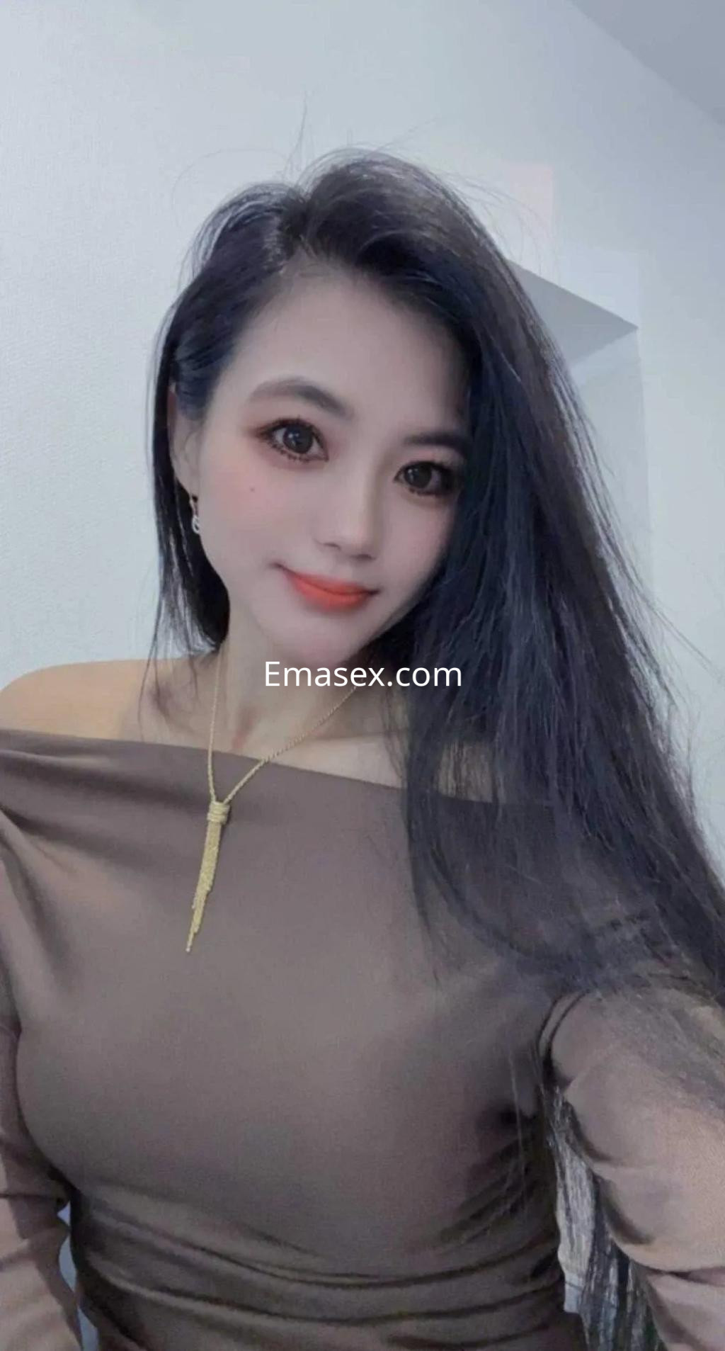 Escort en Madrid, con cabello largo y oscuro, viste una blusa de manga larga marrón y lleva joyería sutil.