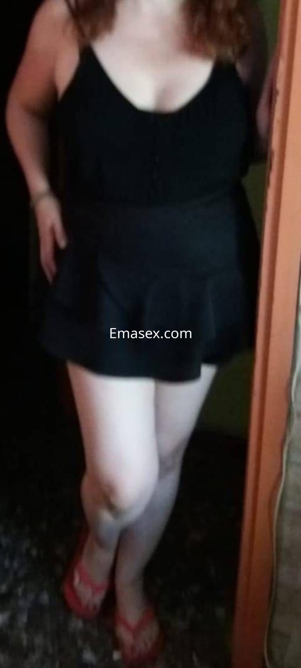 Escort en Barcelona luciendo un top negro sin mangas y una falda corta, con sandalias rosas.