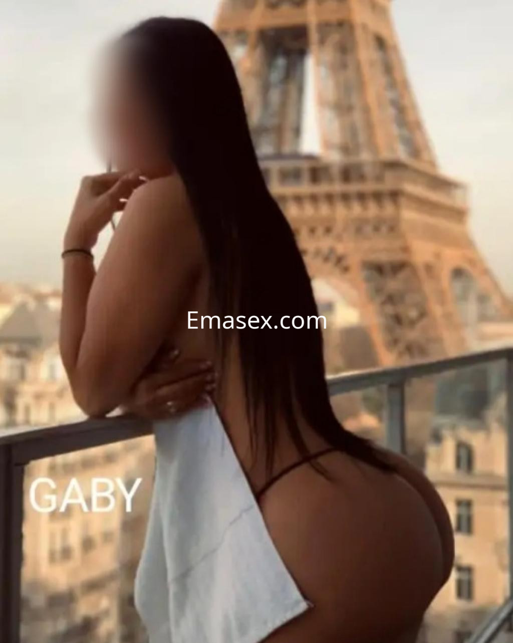 Escort en Lugo posando de espaldas con una toalla blanca, frente a la Torre Eiffel al atardecer.