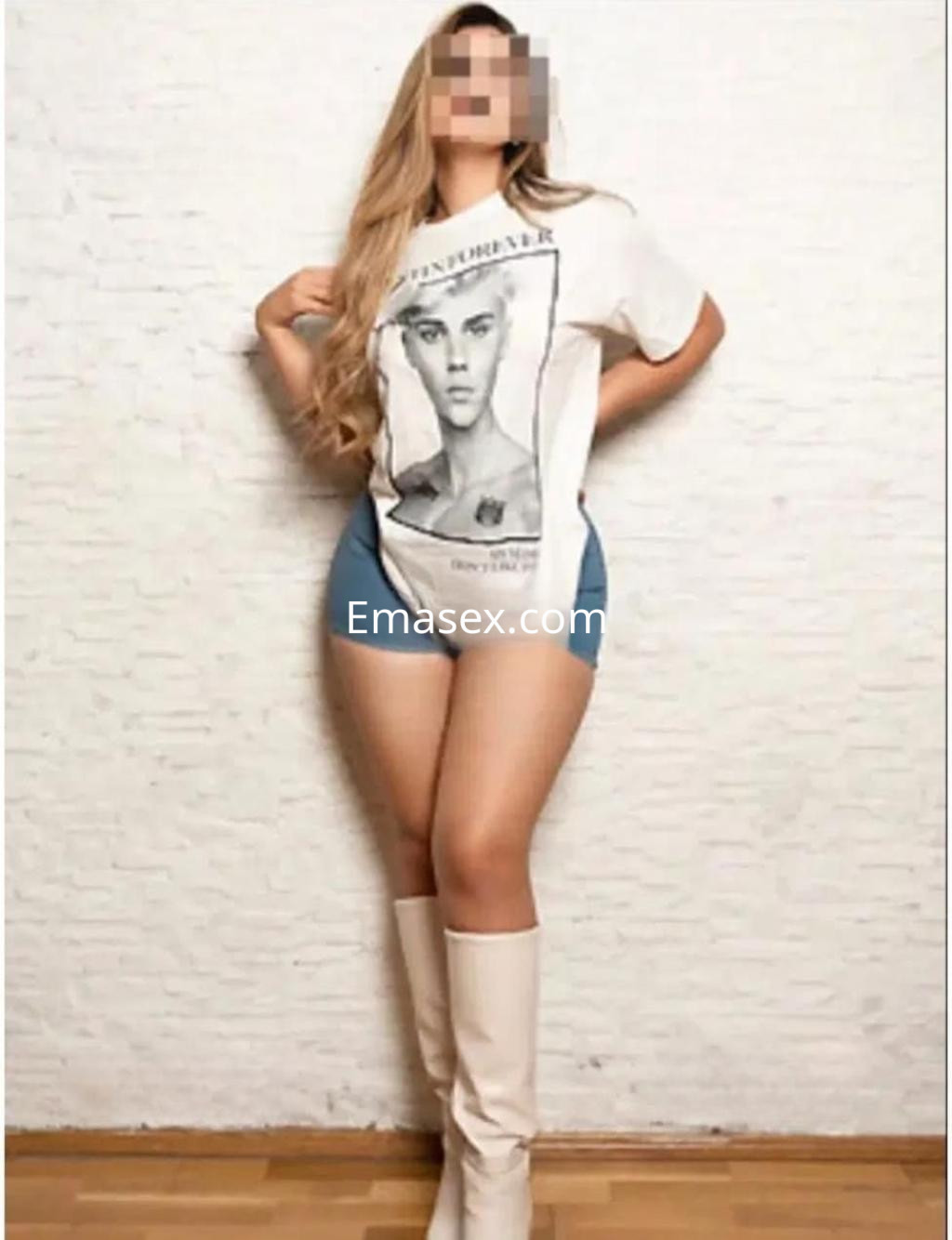 La puta en Granada lleva una camiseta blanca con un diseño gráfico y shorts de mezclilla, luciendo botas altas.