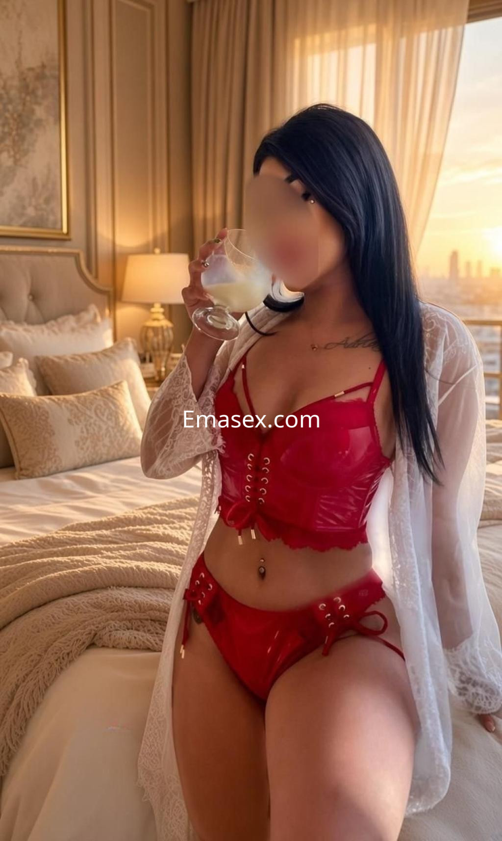 Escort en Málaga viste lencería roja brillante y una bata blanca, sosteniendo un vaso en un entorno elegante.