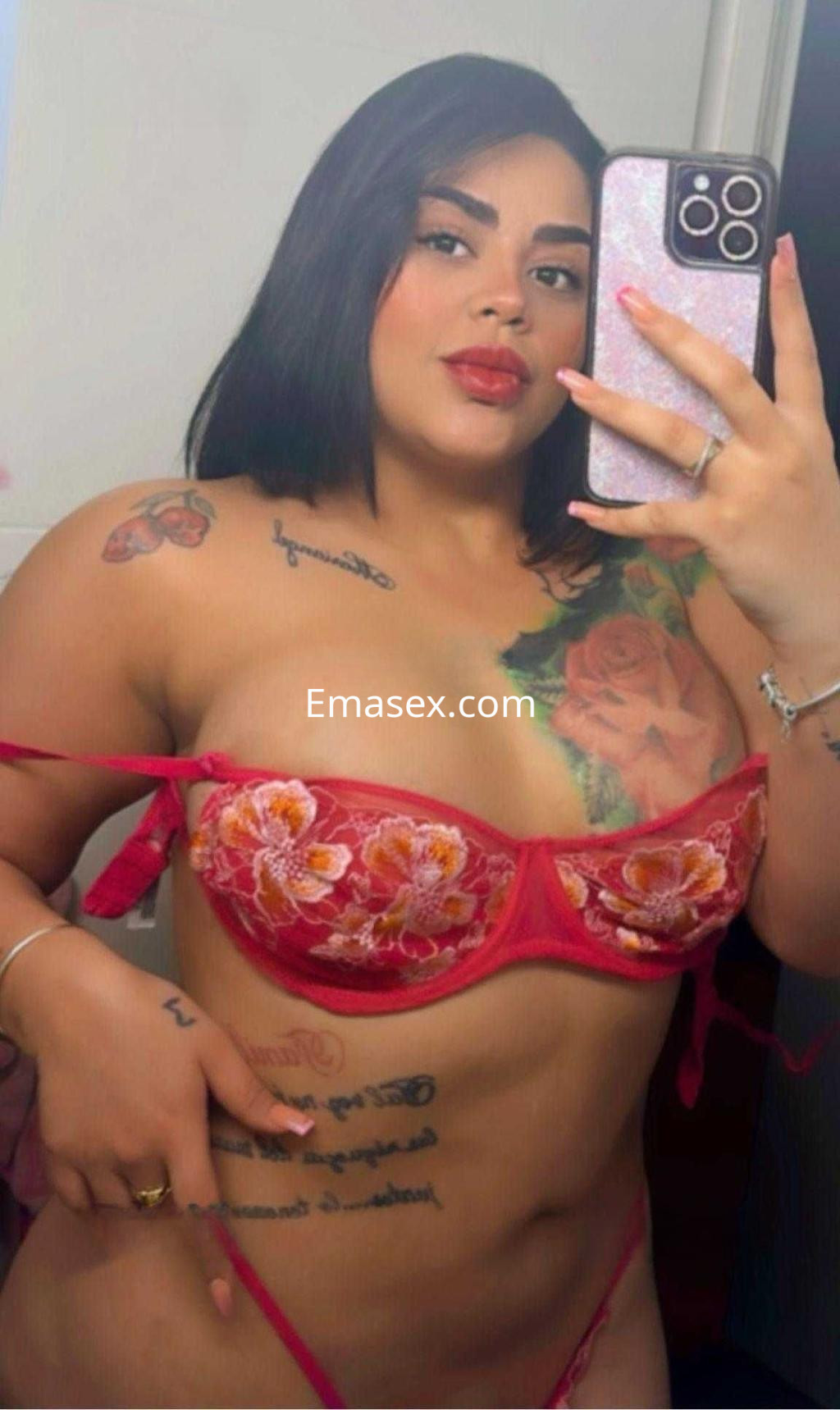 Escort en Málaga luciendo un conjunto de lencería roja con bordados, mostrando sus tatuajes en un espejo.