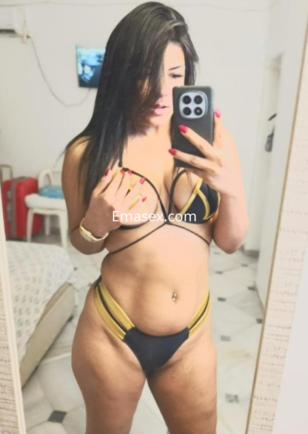 Escort en Sevilla posando en un espejo con lencería negra y dorada, mostrando su cabello largo y oscuro.