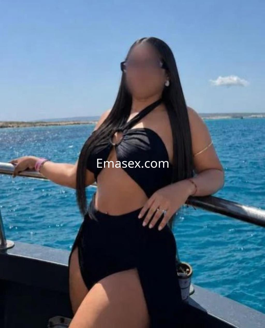 Escort en Madrid luciendo un bañador negro con un diseño distintivo, posando junto al mar en un ambiente soleado.