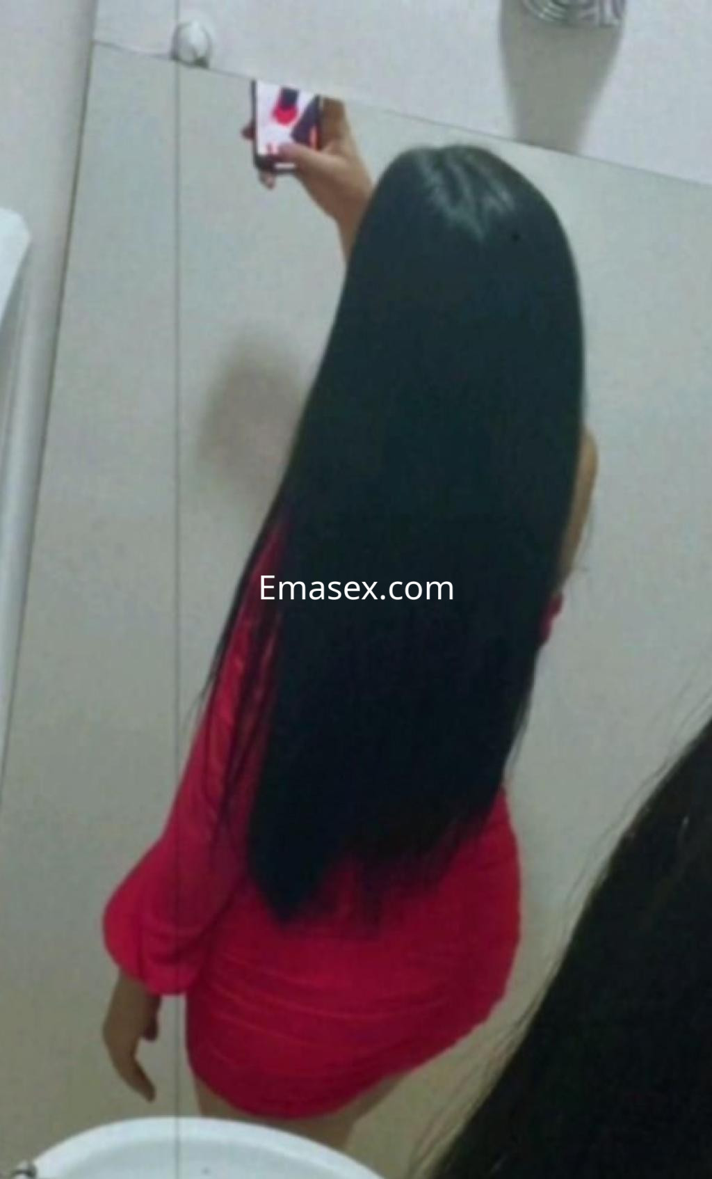 Escort en Murcia, tomando una selfie en el espejo, vistiendo un vestido ajustado de color rosa y con cabello largo y negro.