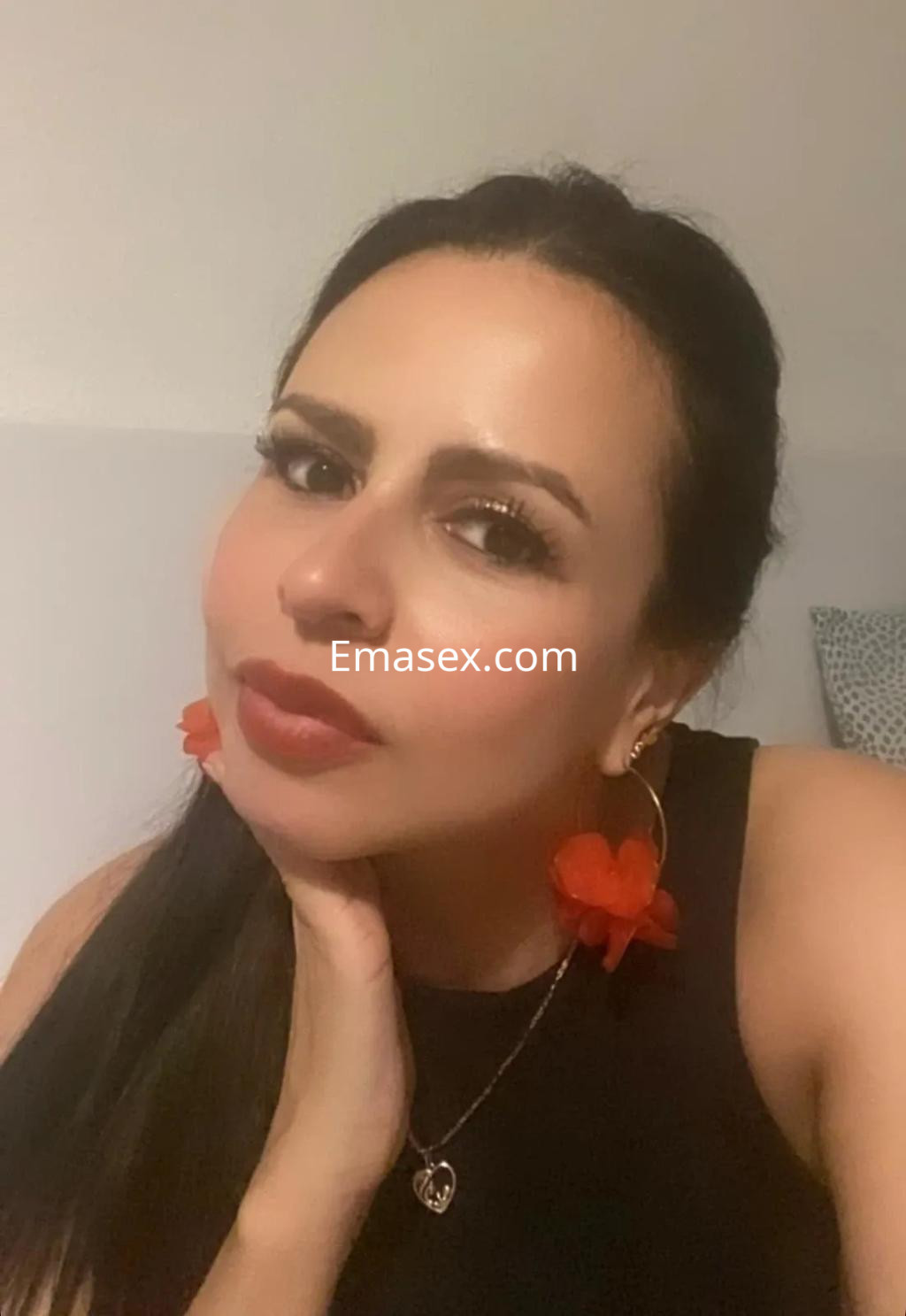 Escort en Valladolid con cabello largo y oscuro, usando pendientes rojos y maquillaje suave, posando con expresión coqueta.