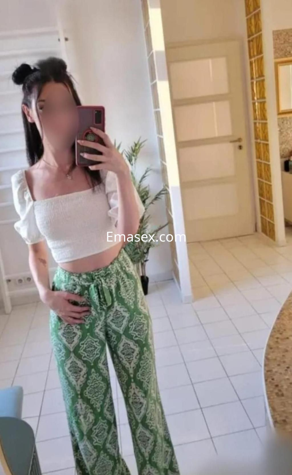 La puta posa en un espejo con una blusa blanca de mangas cortas y pantalones verdes en Zaragoza.