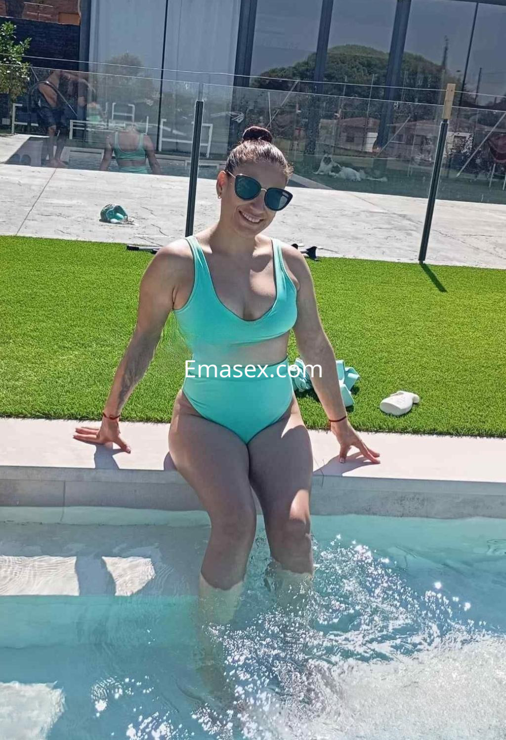 La puta se sienta en el borde de la piscina, vistiendo un bañador verde claro, en un día soleado en Alicante.
