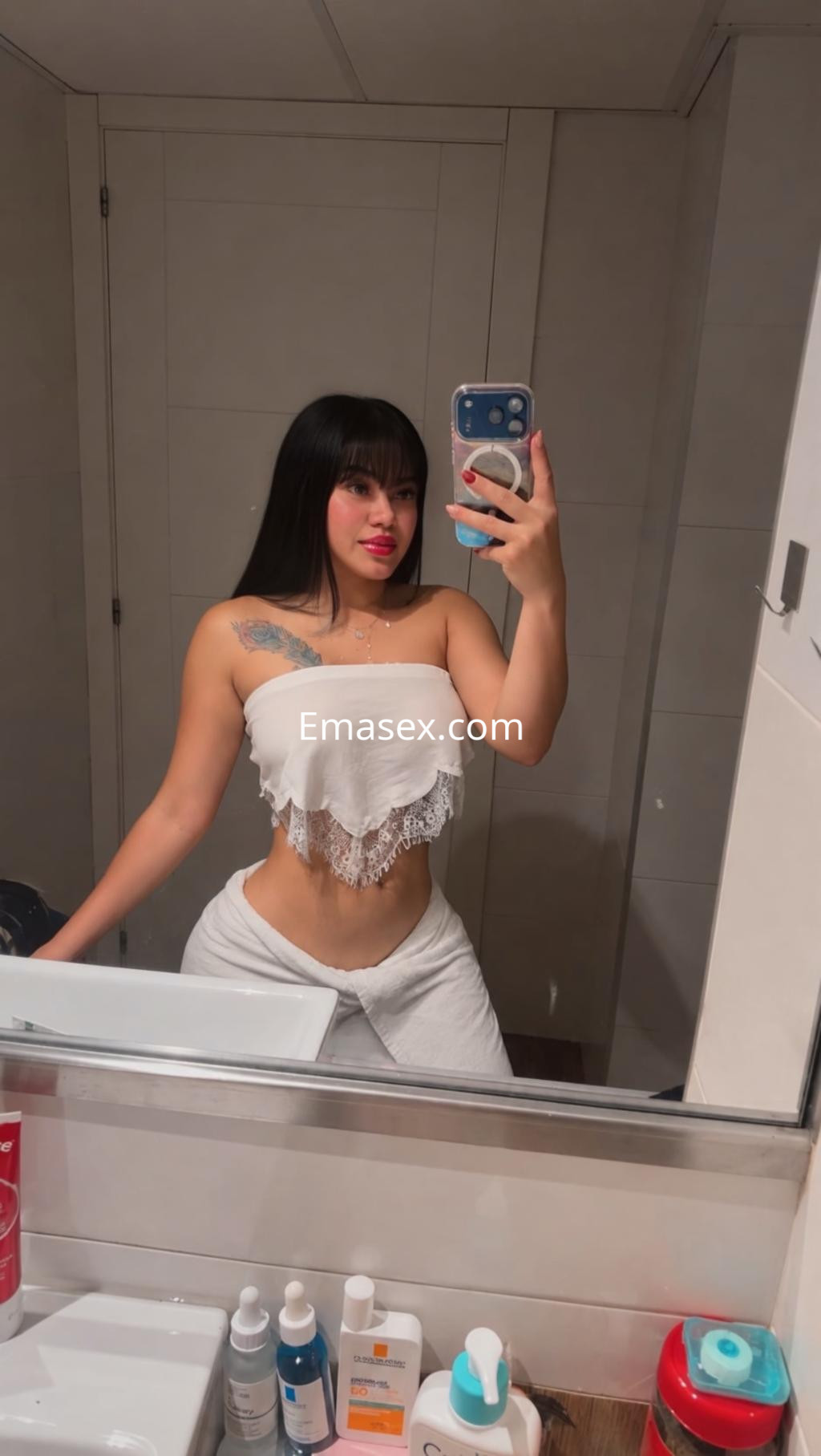 Escort en Zaragoza, luciendo un top blanco sin mangas y pantalones claros, posando frente a un espejo.