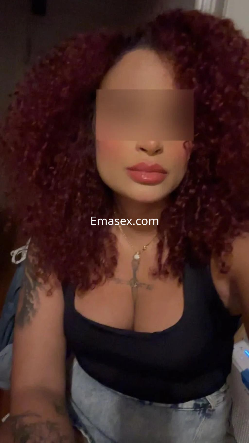 Escort en Madrid con cabello rizado y colorido, usando una blusa negra y mostrando un collar dorado.
