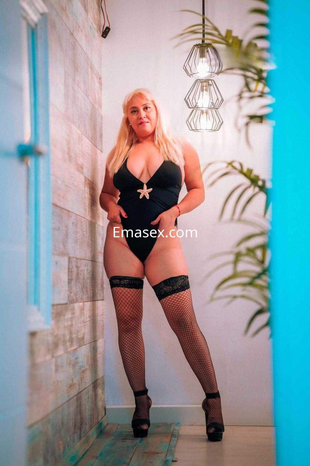 La puta luce un body negro con detalles en la cadera y medias de rejilla, posando en un entorno moderno en Toledo.
