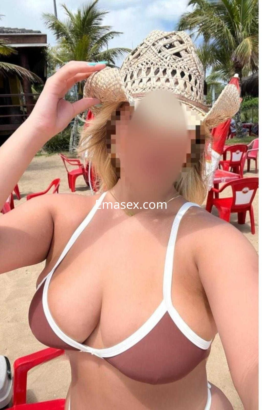La puta posa en la playa de Málaga, vistiendo un bikini marrón y un sombrero de paja, luciendo segura.