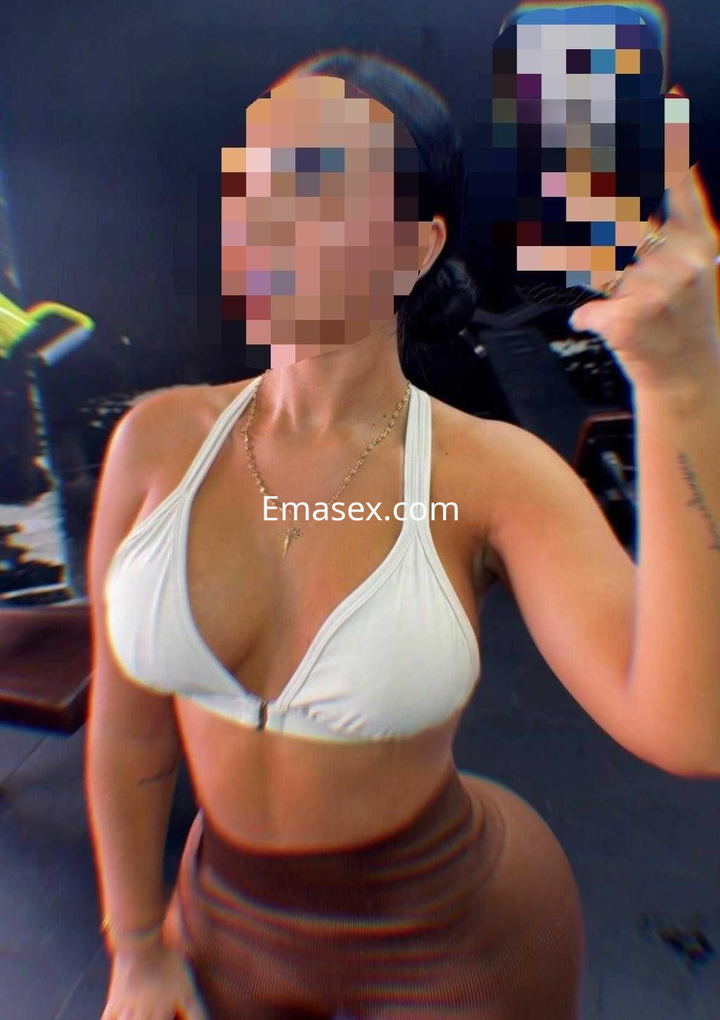 La escort en Málaga viste un top blanco y leggings ajustados, mientras se toma una selfie en un gimnasio.