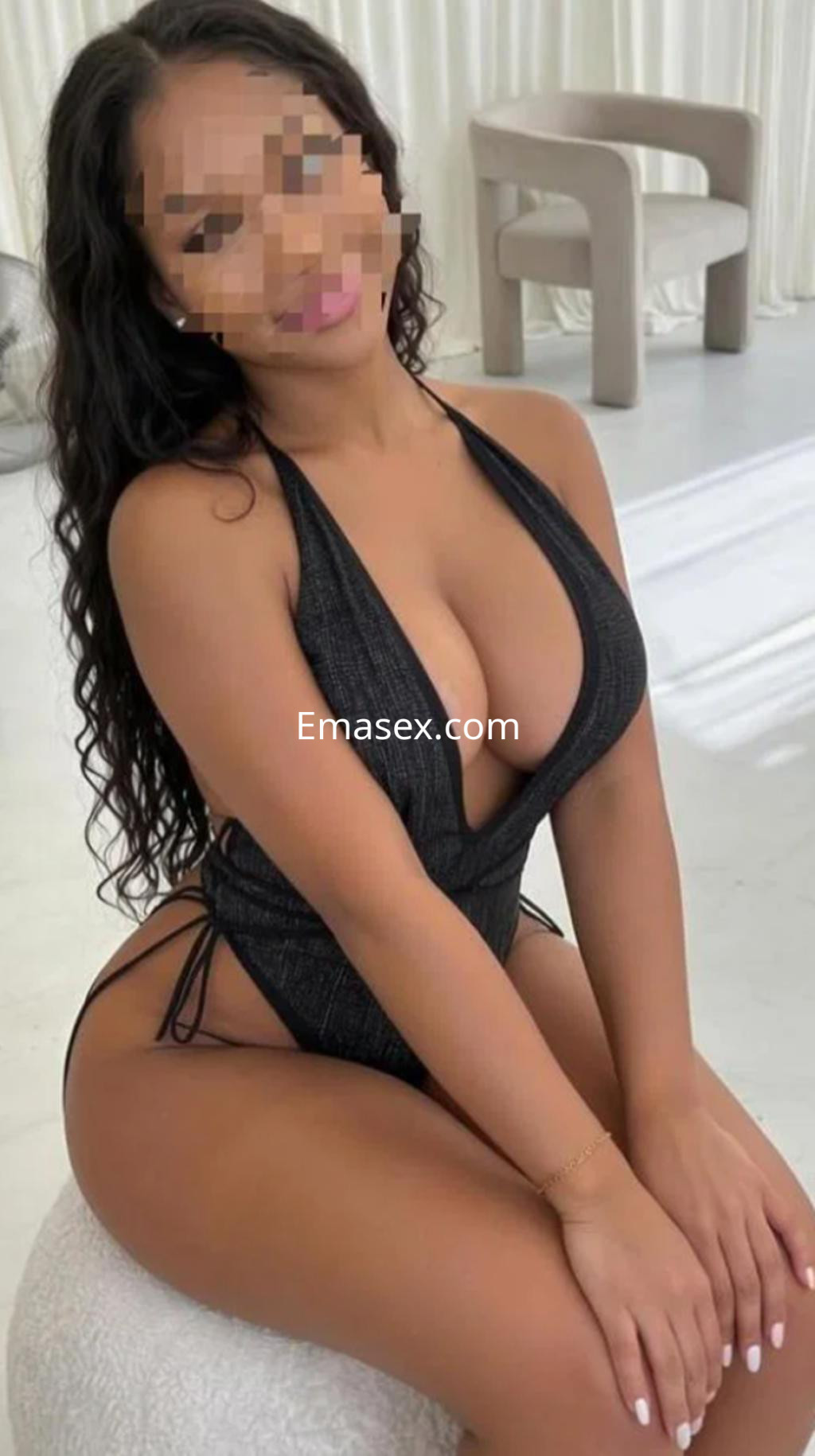 Puta sentada en un taburete, con un bañador negro y cabello largo y rizado, en un entorno luminoso en Vitoria.