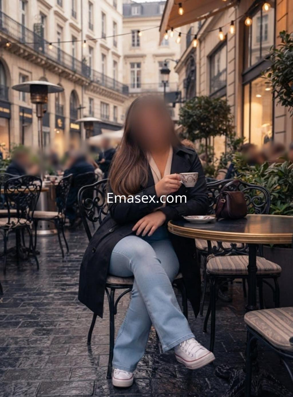 Escort en Bilbao sentada en una terraza con una taza en la mano, vistiendo un abrigo negro y jeans claros.