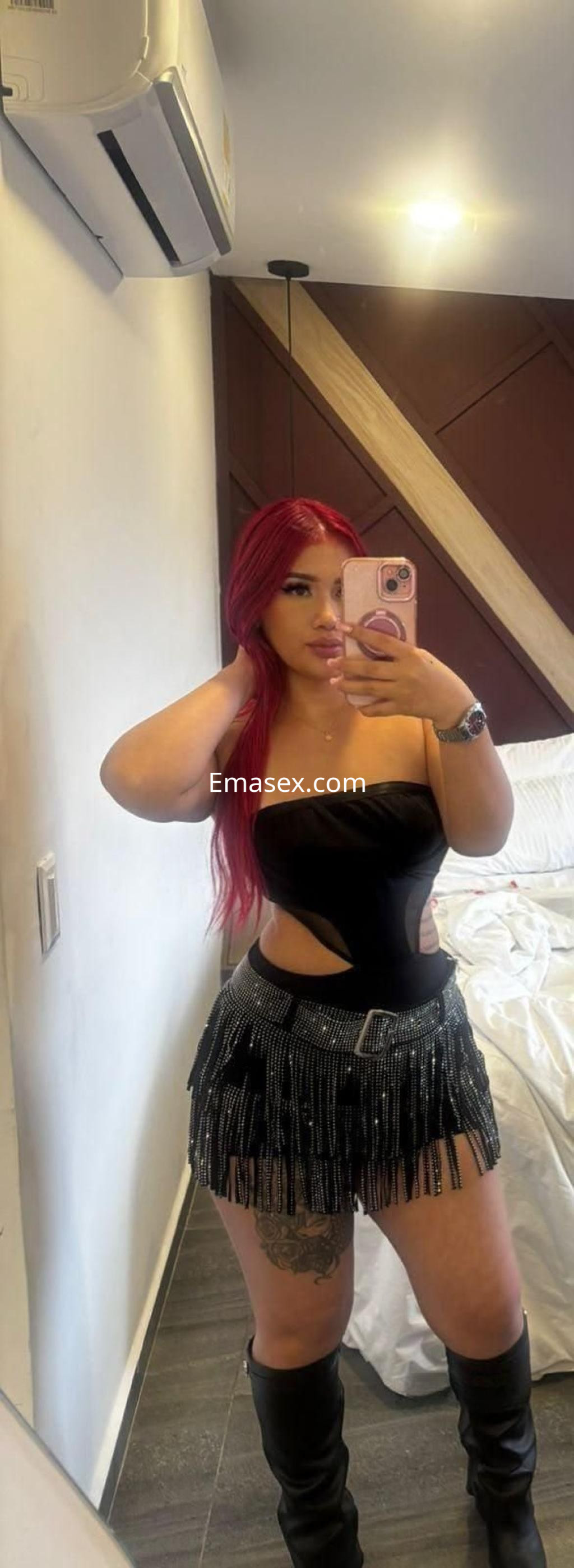 Escort en Madrid con cabello largo y rojo, vestida con un top negro y falda con flecos, posando en un interior moderno.