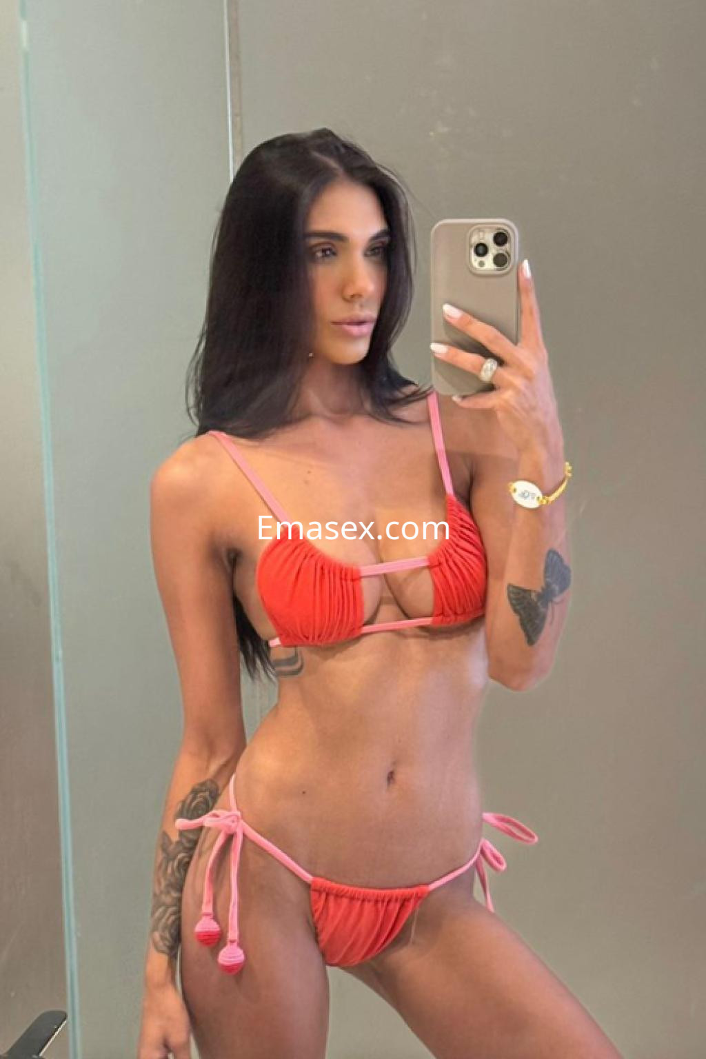 Escort en Ibiza, posando frente al espejo con un bikini rosa y negro, mostrando su cabello largo y lacio.