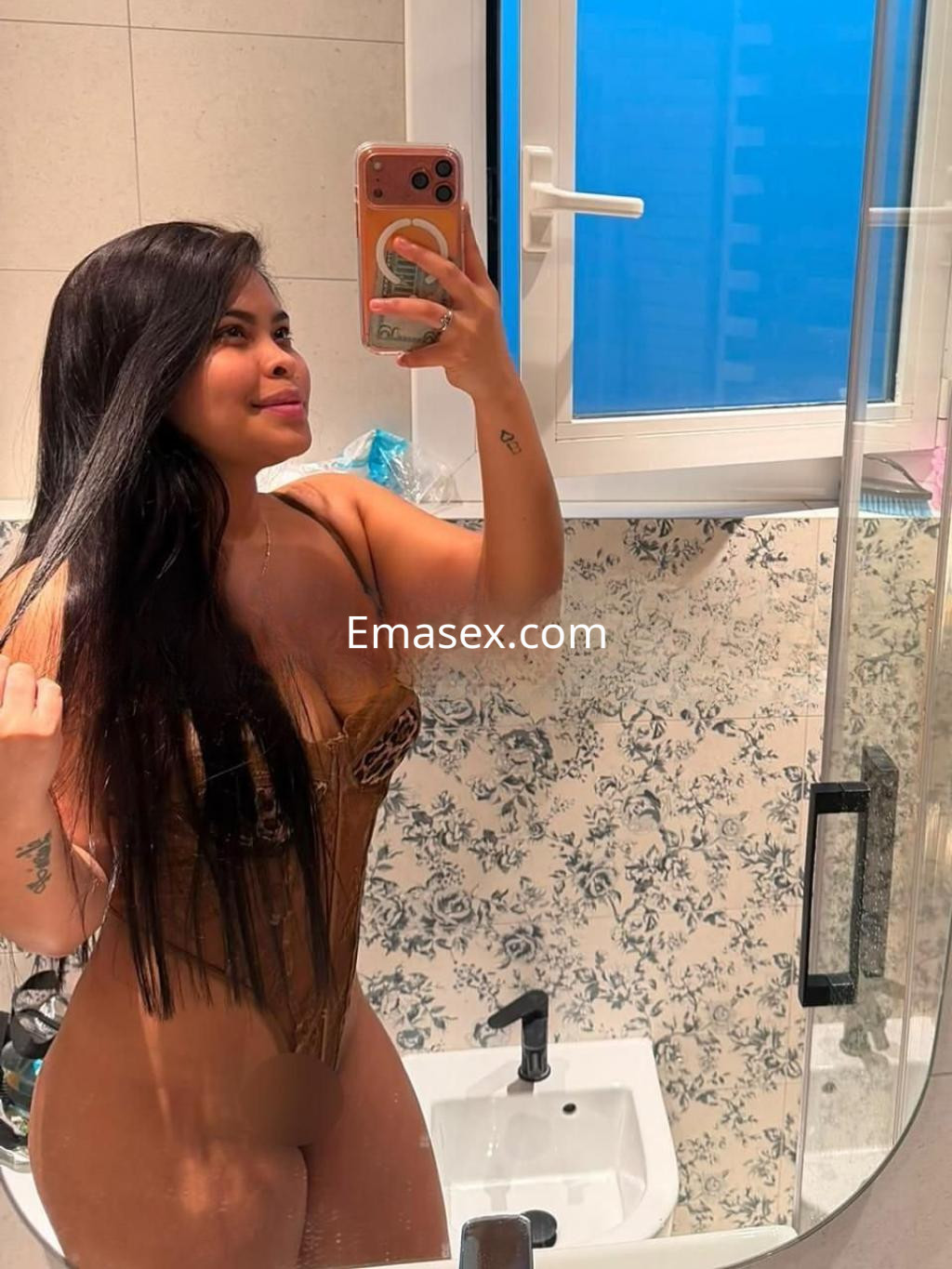 Puta con cabello largo y lacio, vestida con un corsé dorado, posando frente a un espejo en un baño de Barcelona.