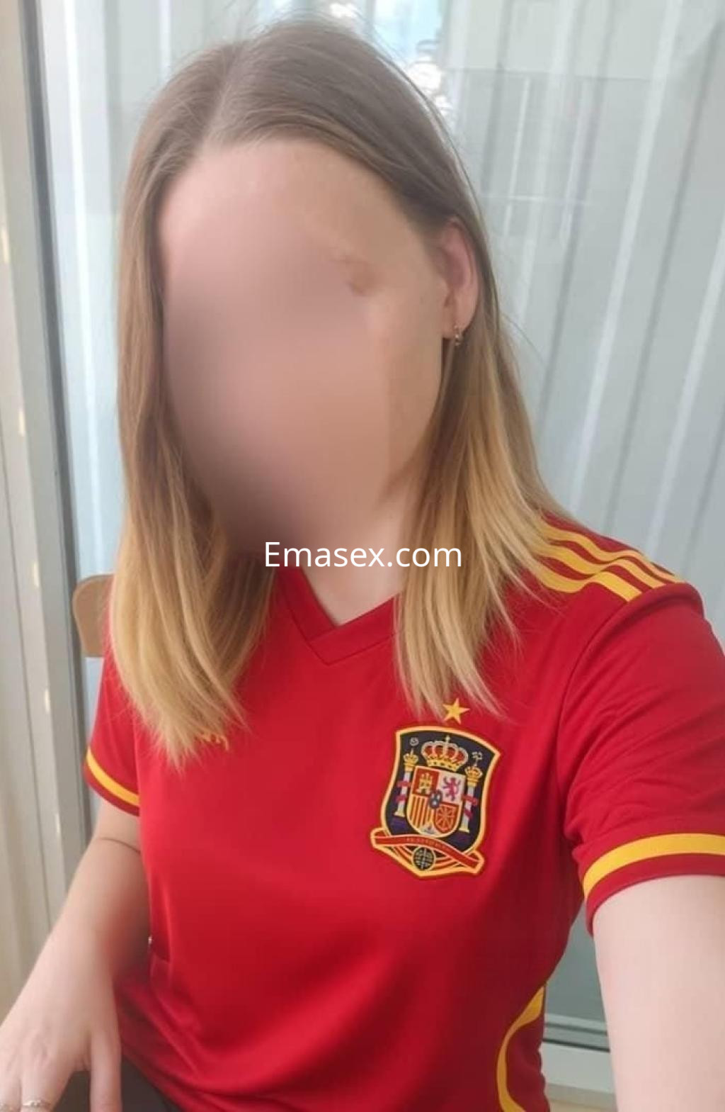 Puta en Valladolid con camiseta roja de la selección española, cabello rubio y fondo de luz natural.