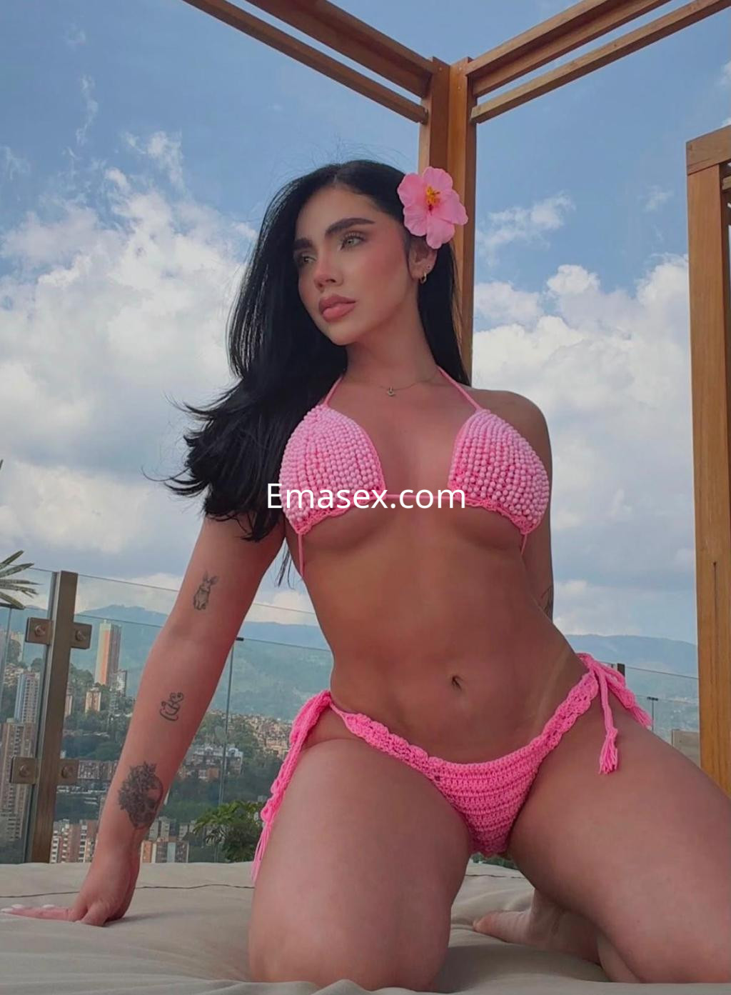Puta posando en una terraza de Santander, luciendo un bikini rosa de crochet y una flor en el cabello.