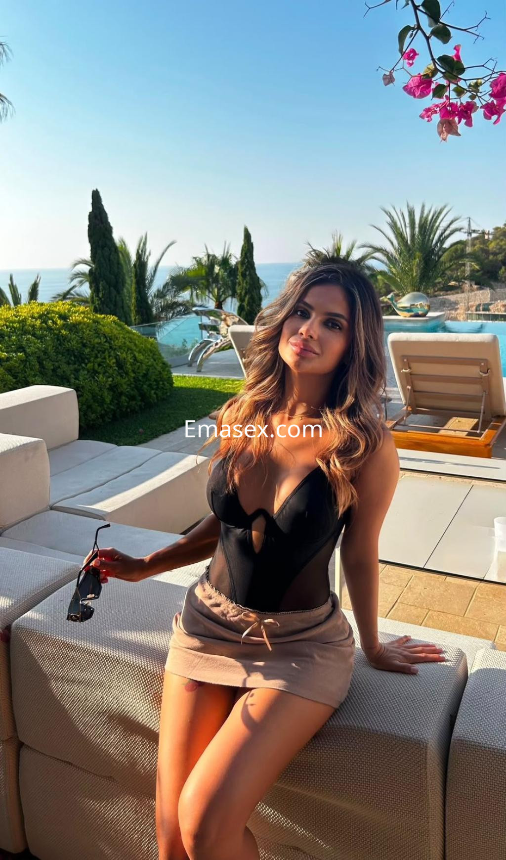 Escort en Ibiza con cabello largo y ondas, luciendo un body negro y una falda corta, posando en un entorno al aire libre.
