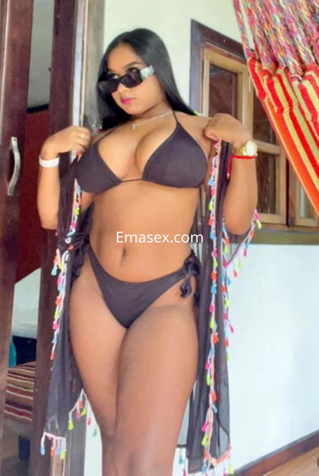Puta en Gijón posando con un bikini negro y un pareo transparente, lleva gafas de sol y tiene el cabello largo.