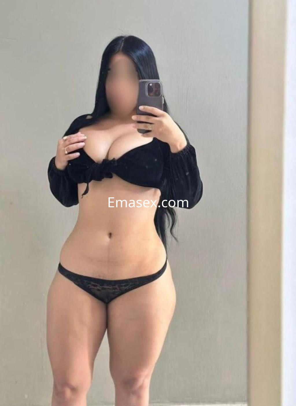 Escort en Madrid posando frente al espejo, vistiendo un top negro y una lencería oscura, con cabello largo.