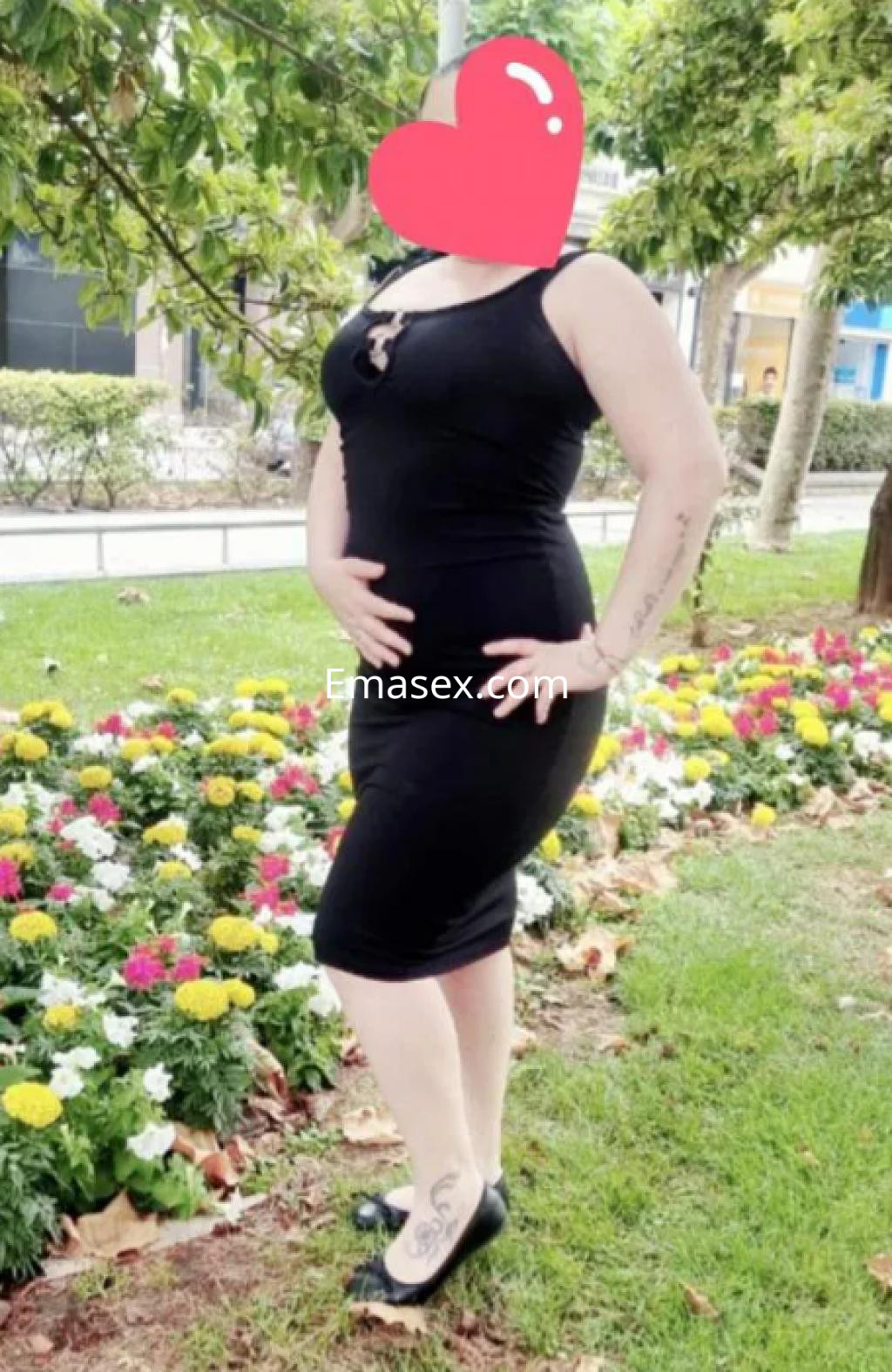 Escort en Logroño vista de pie, luciendo un vestido negro ajustado y tacones, con flores coloridas de fondo.