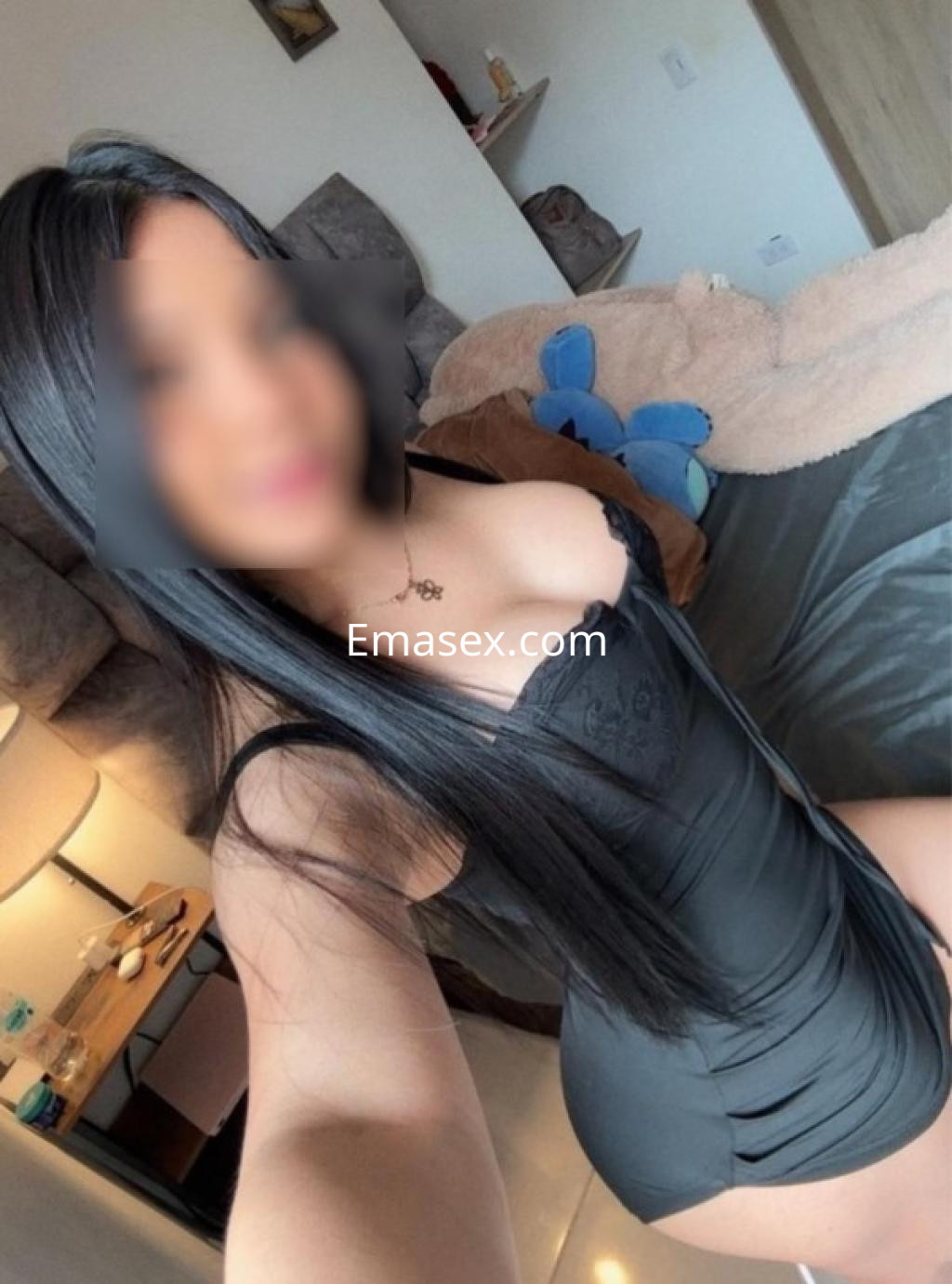 Escort en Santander viste un body negro ajustado, con cabello largo y lacio, posando en un ambiente acogedor.