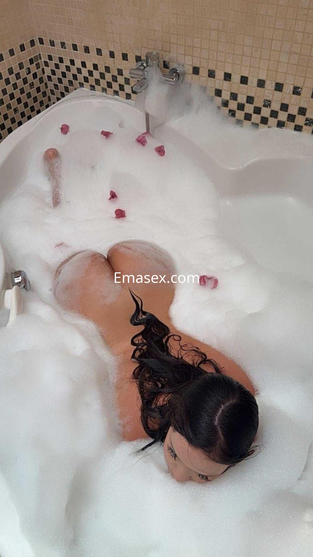 Puta sumergida en una bañera llena de espuma, con pétalos de rosa y cabello largo y oscuro, en Toledo.