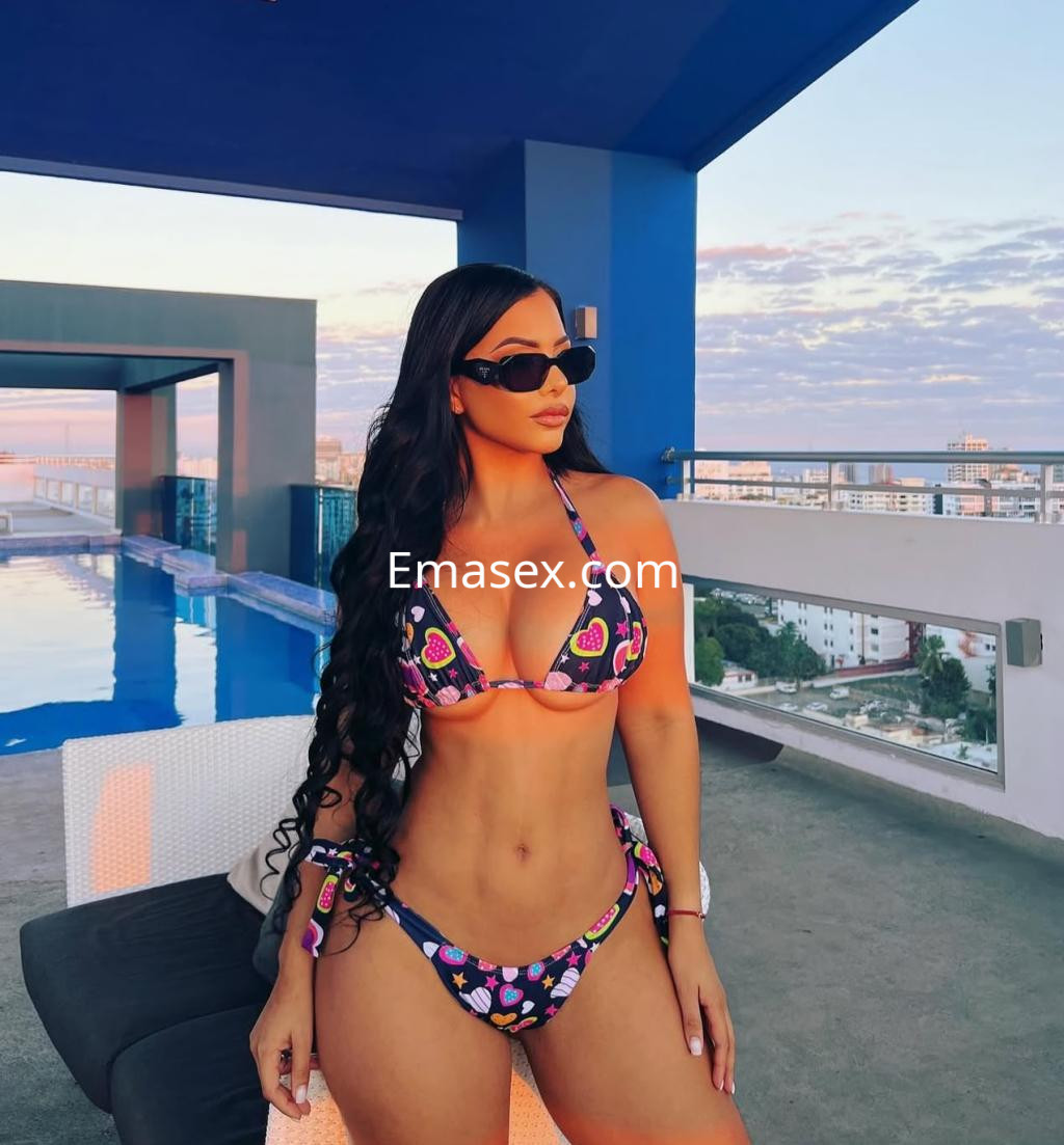 La puta posa en una piscina de Valladolid, luciendo un bikini colorido y gafas de sol, con el cabello largo y ondulado.