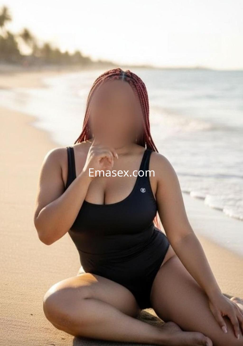 Puta posando en la playa de Tarragona, con un bañador negro y trenzas rojas, sentada sobre la arena.