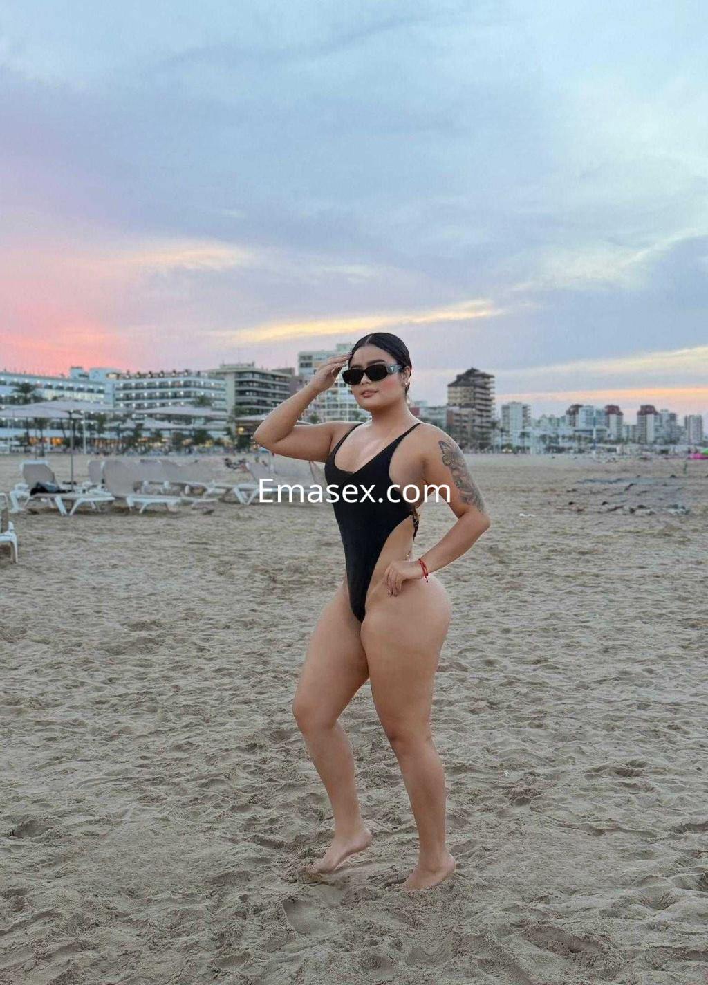 La puta luce un bañador negro y gafas de sol mientras posa en la playa de Castellón al atardecer.