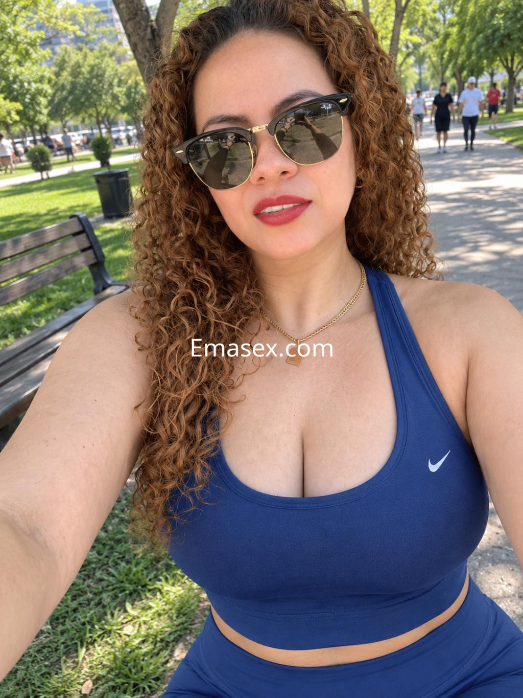 Puta con cabello rizado y suelto, vistiendo un top deportivo azul, posando en un parque en León.